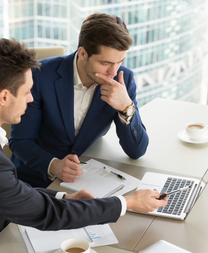 Business partners using laptop while working together on important corporate project in office. Businessman attentively listening to adviser Investment specialist making presentation of promising deal
